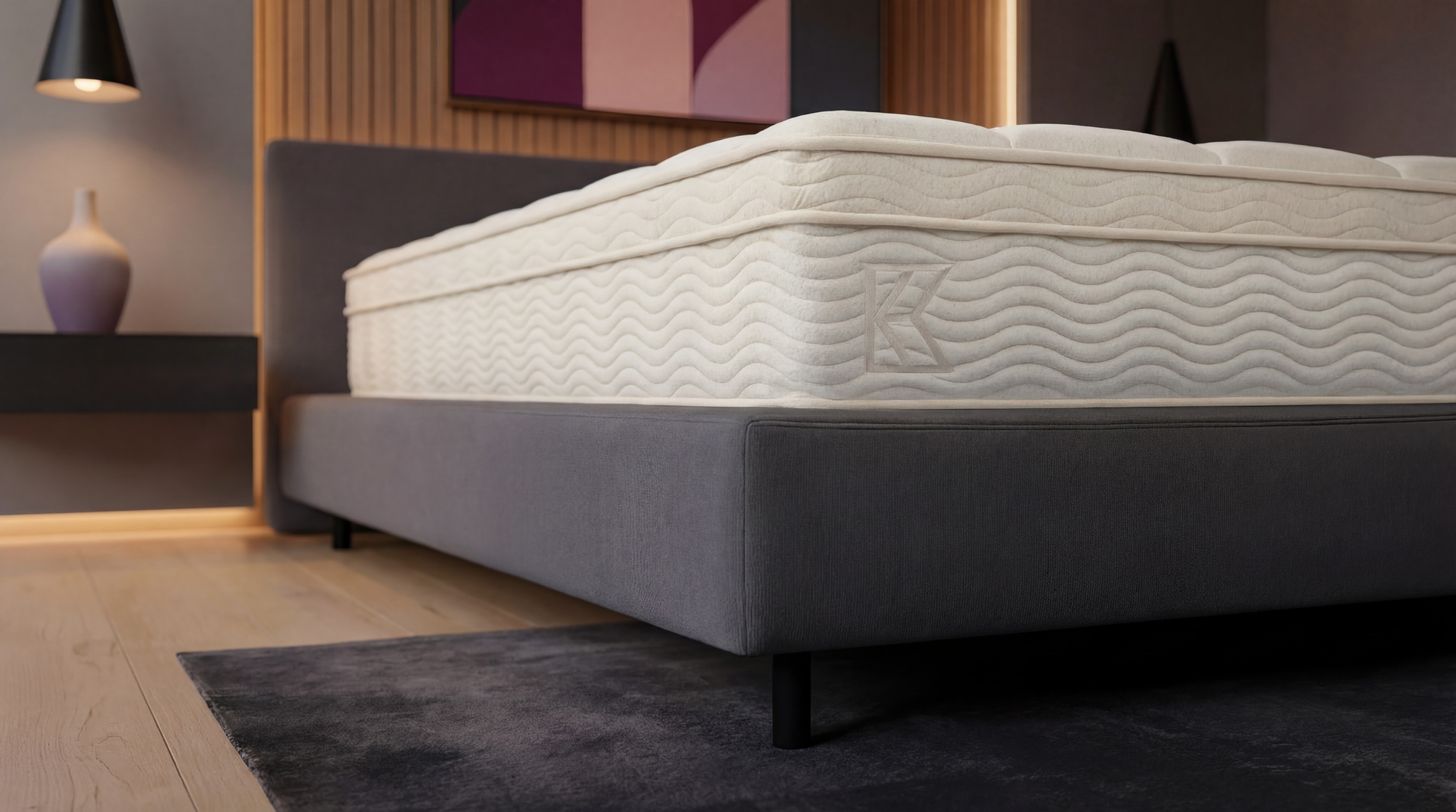 Close-up of Keetsa Tea Leaf Classic mattress on a gray upholstered base, featuring a cream cover with wave stitching and subtle K logo, emphasizing edge support, durable materials, and consistent comfort across the sleep surface.