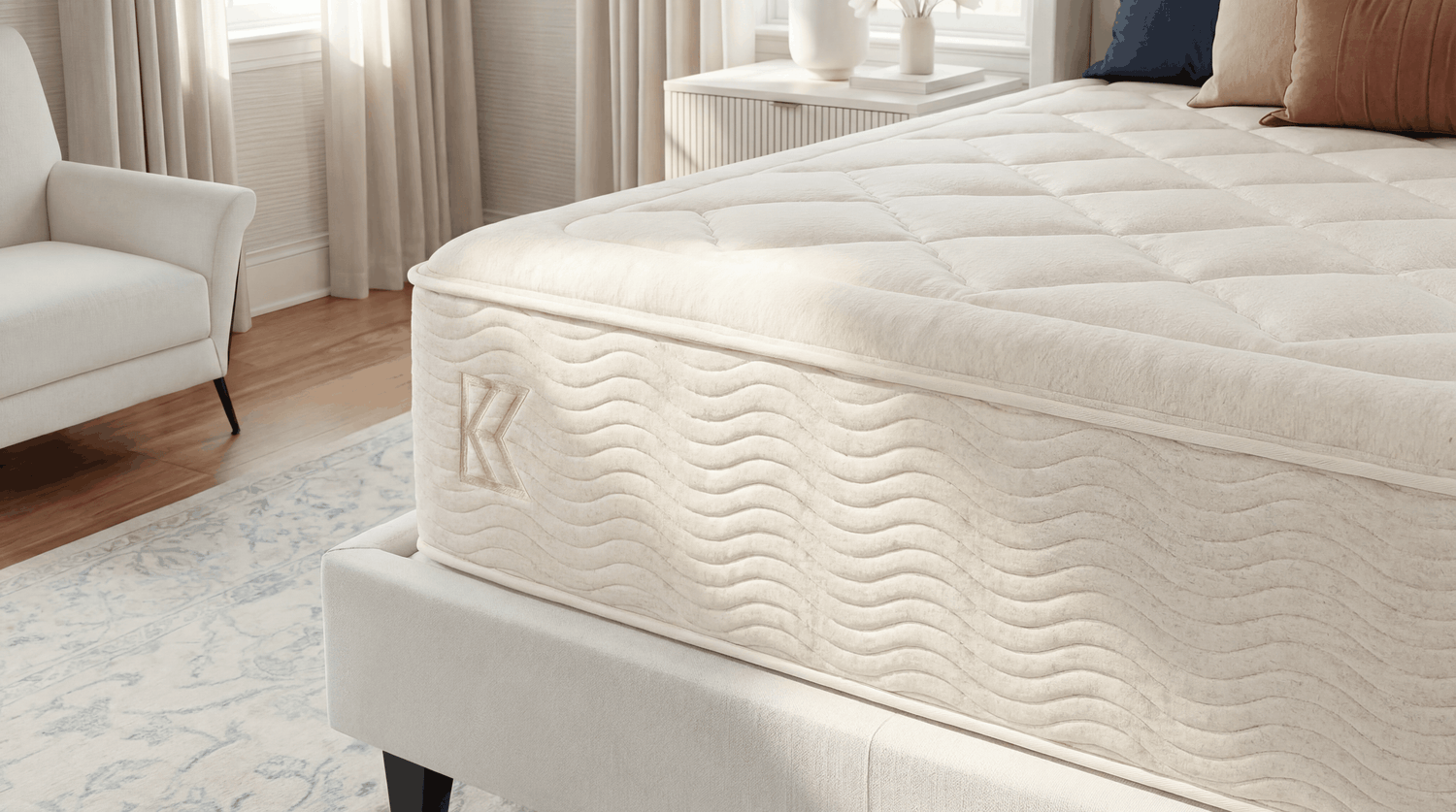 Close-up corner of Keetsa Dream mattress showing diamond-quilted sleep surface, wave-stitched side panel, embossed Keetsa logo, and structured pillow-top edge on upholstered platform base.