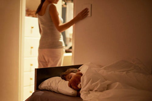 Mother turning off light as boy sleeps in bed with non-toxic bedding