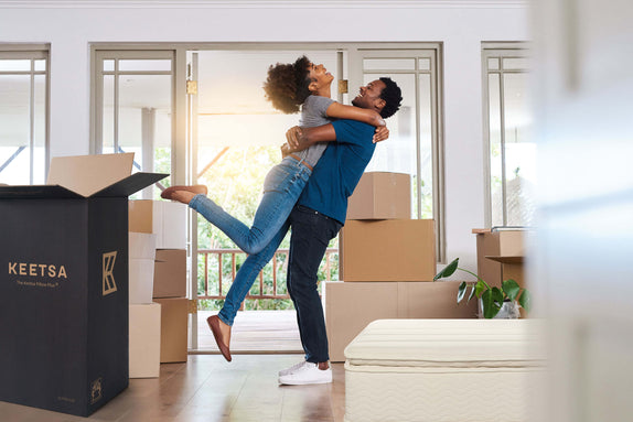 A couple is hugging and smiling in their new home with a Keetsa mattress.