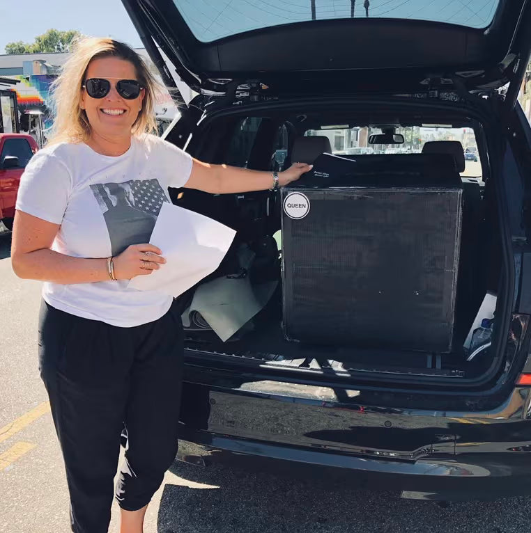 Smiling customer holding her paperwork beside a Keetsa mattress box loaded in an SUV