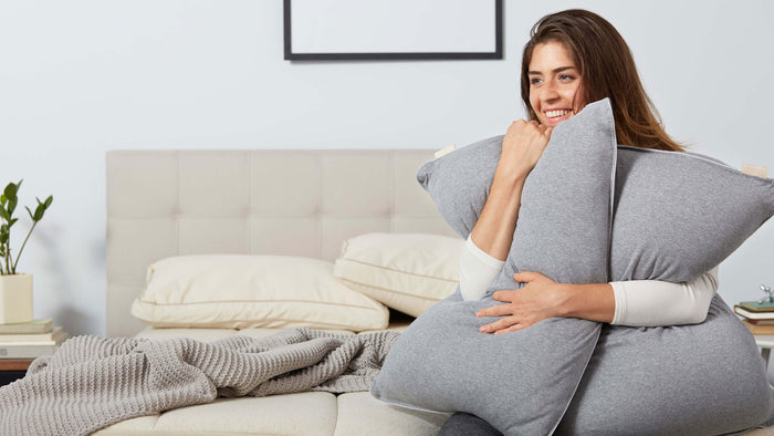 Welcome to the pillows page. Woman is hugging a pillow and smiling comfortably on the Keetsa mattress.