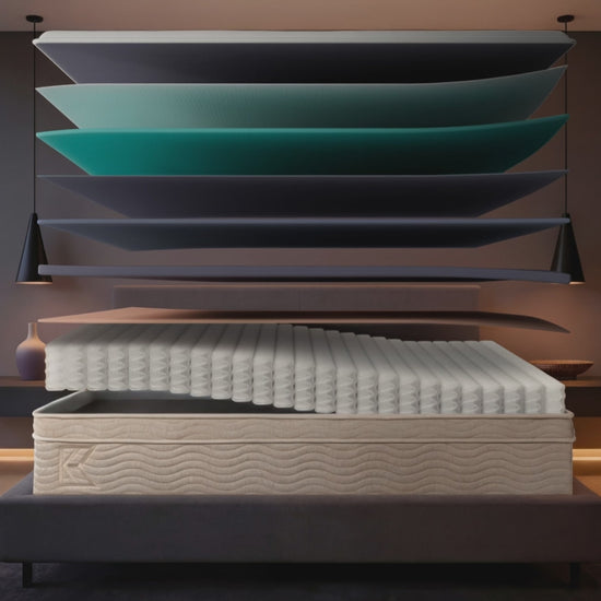 Keetsa Classic firm hybrid mattress animation: separated foam and individually wrapped coil layers float above a gray upholstered platform bed, then settle into the finished 13-inch mattress in a city bedroom at dusk.