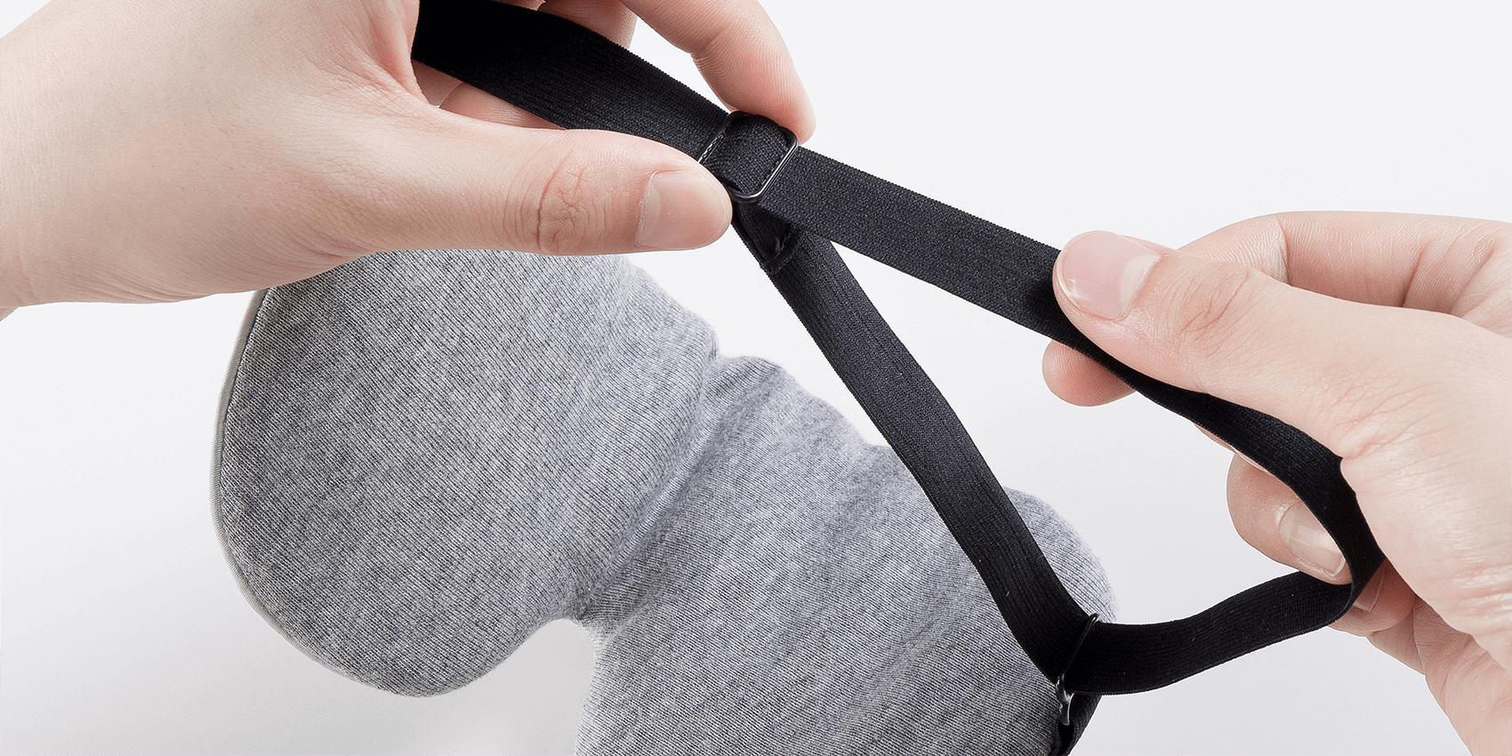 Keetsa sleep eye mask close-up of hands adjusting black elastic headband with sliding buckle for custom fit, showing gray jersey knit mask body.