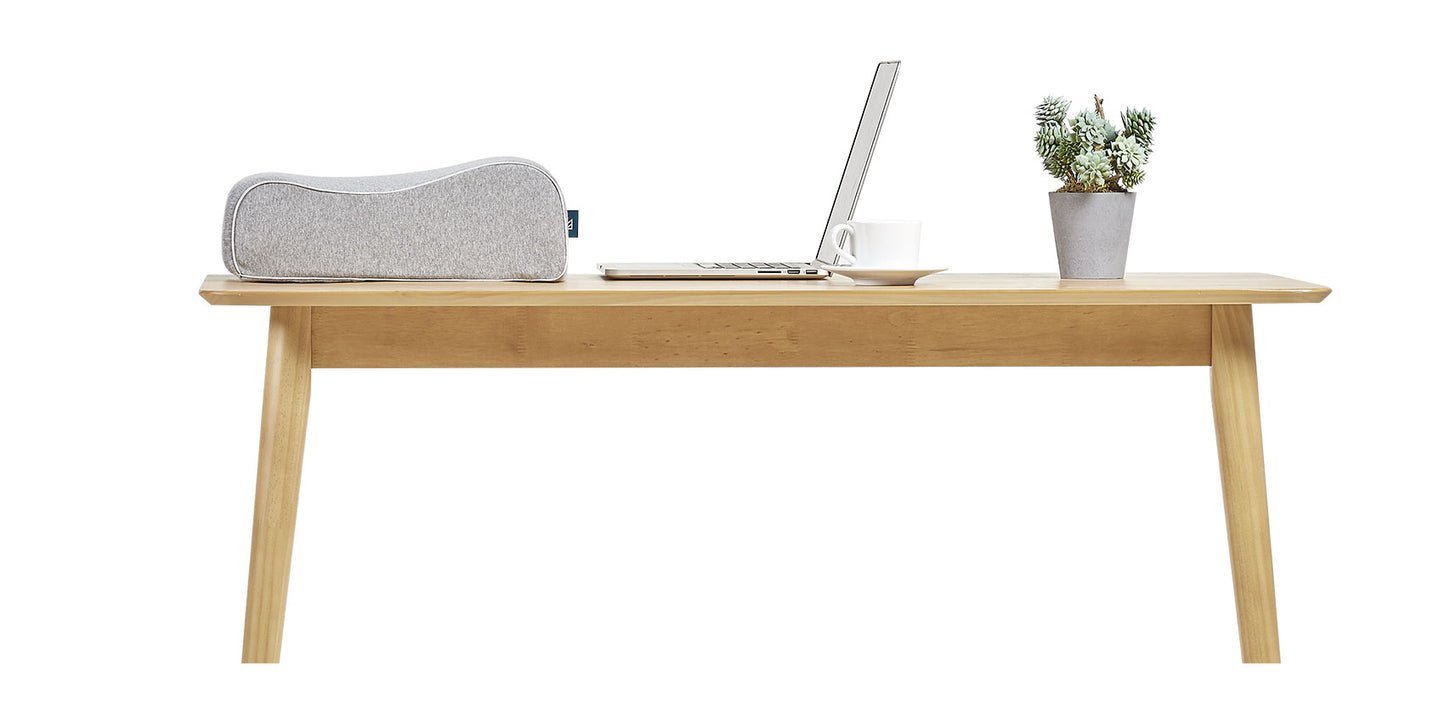Keetsa Siesta pillow in heather gray with contoured ergonomic shape displayed on wooden desk beside laptop, coffee cup, and plant, showing compact portable size for office napping.