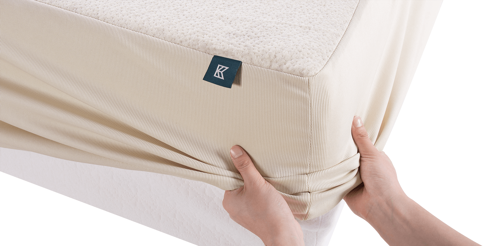 Keetsa waterproof mattress protector being fitted onto mattress by hand, showing stretchy ribbed skirt with deep pocket design, branded Keetsa tag, and textured hemp top surface.